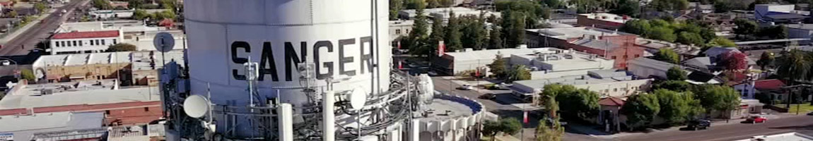 A big white water tower with the city name "Sanger" surrounded by satellites and industrial buildings