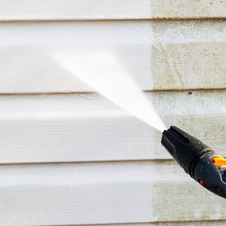 a blast of water from a hose nozzle sprays on a white house cleaning off dirt and grime