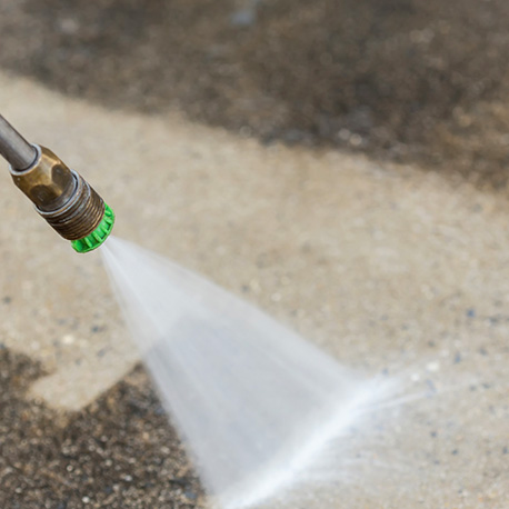 a triangular water high pressure stream of water comes from a hose onto concrete cleaning off years of buildup