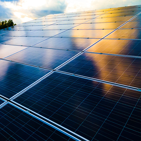 a grid of very clean solar panels on a steep roof reflect the clouds and sun