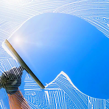 a window with soap as a hand cleans the window with a squeegee on a sunny day with a blue sky